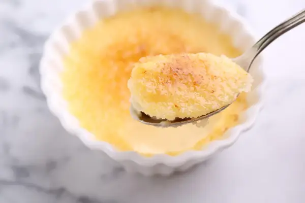 Une cuillère de semoule au lait et aux œufs, avec sa croûte caramélisée dorée, prête à être dégustée.