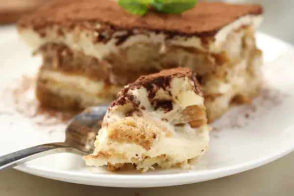 Une part de tiramisu, avec ses couches de crème et de biscuit cuillère, saupoudrée de cacao.