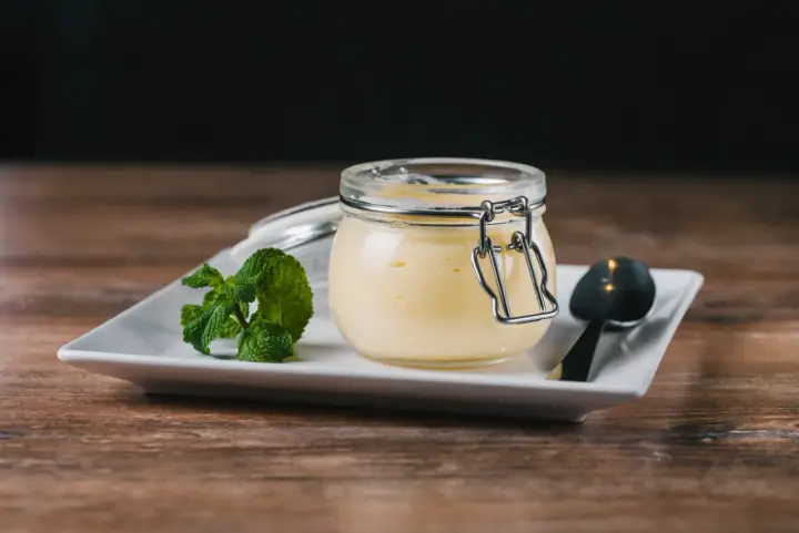 Un pot de crème anglaise, garni de menthe fraîche, sur une assiette blanche avec une cuillère. Un délice simple.